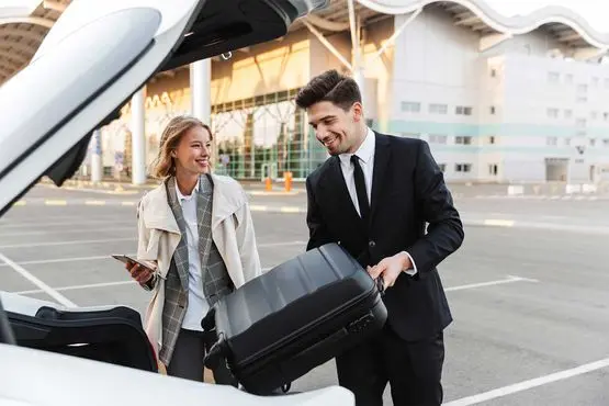 Chauffeur chargeant les bagages d'une voyageuse devant un aéroport